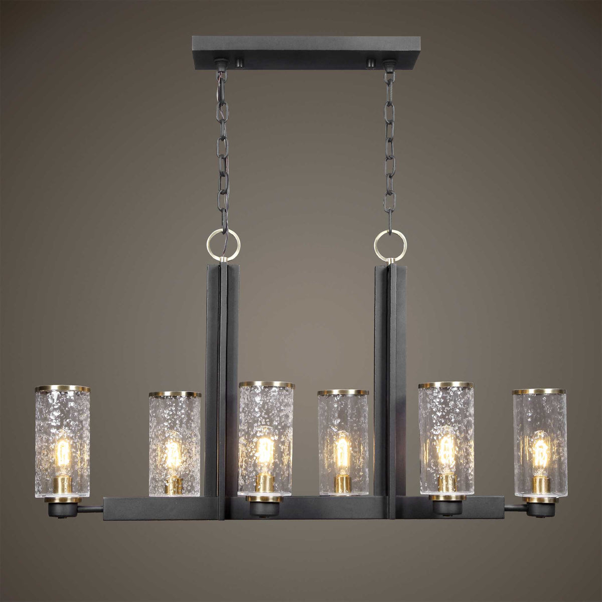 Jarsdel black and brass island light with clear glass, lit against a taupe wall