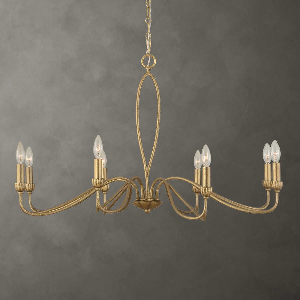 Corella gold chandelier with looped petal arms against a gray plaster backdrop