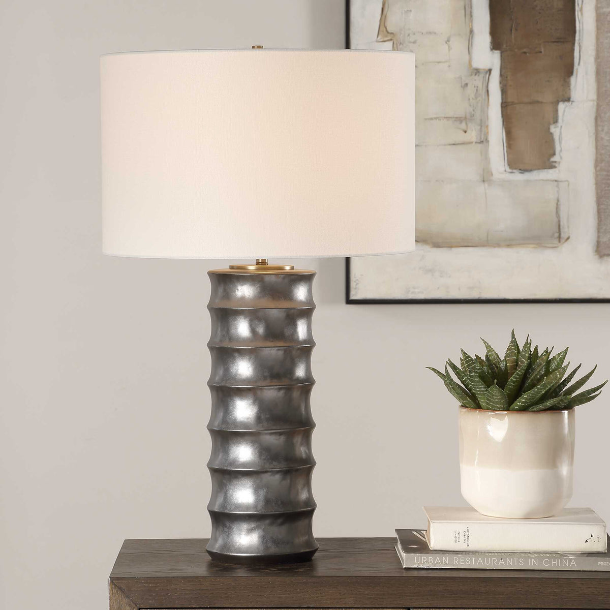Corvair scalloped porcelain table lamp on a wood dresser beside a potted plant and stacked books
