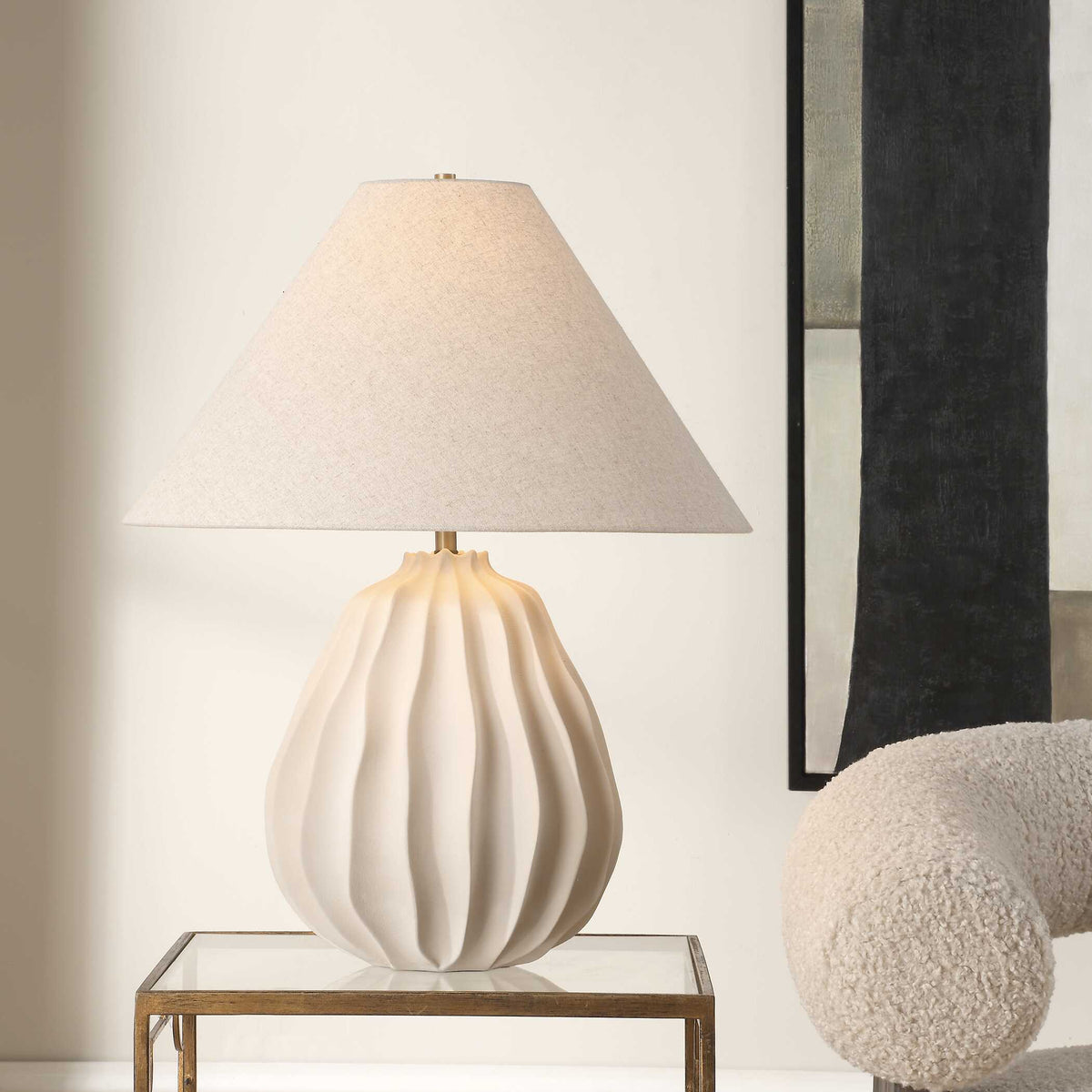 Javary white porcelain table lamp on a glass and brass side table beside a cream boucle ball pillow