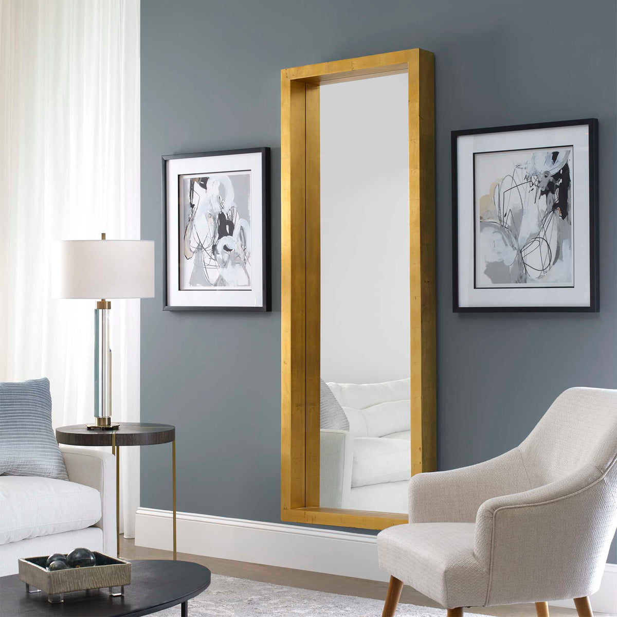 Uttermost 14554 Edmonton gold leaner mirror against a gray wall between framed art prints