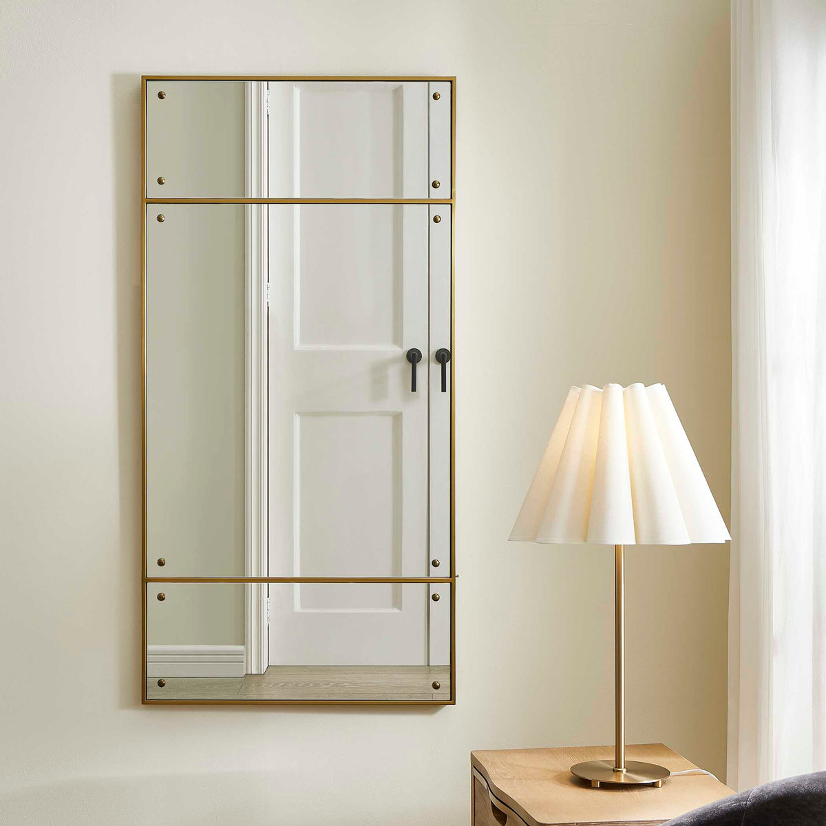 Uttermost 08252 Wrenton collection brass mirror on an entry wall beside a bedside table and lamp