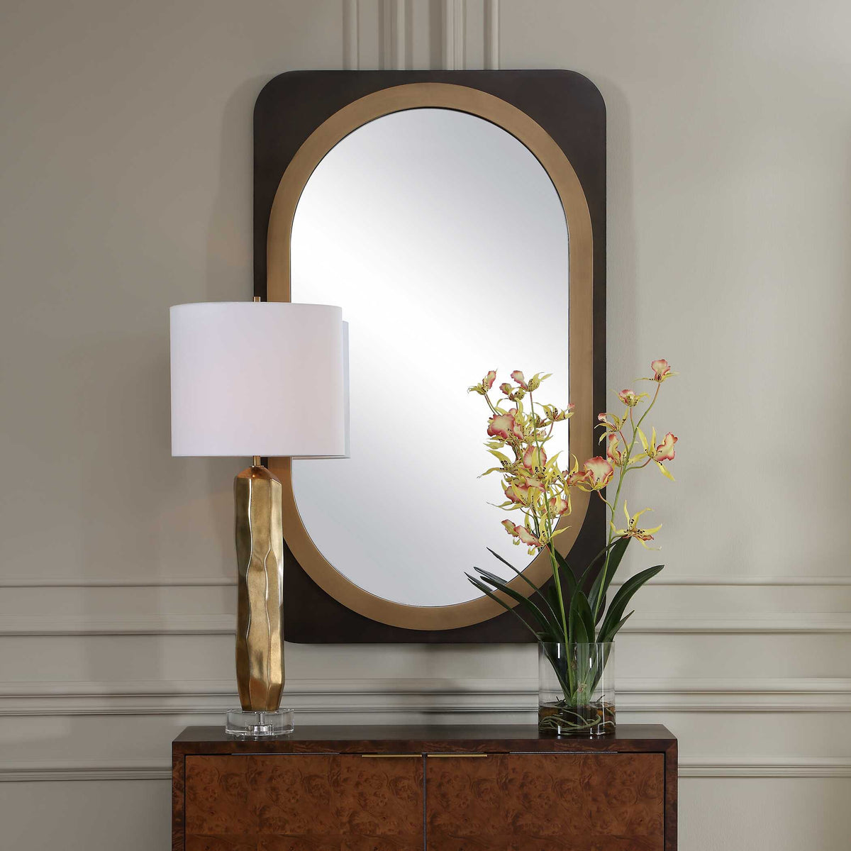 Uttermost 08377 Condesa collection mirror above a burl cabinet with a gold lamp and orchids