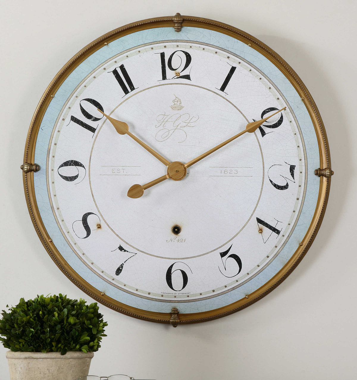 Torriana antiqued gold wall clock with a blue band above a potted boxwood