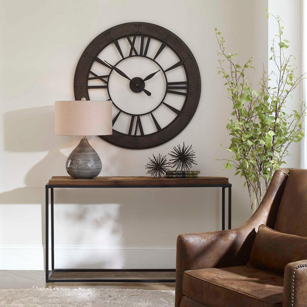 Ronan bronze wall clock above a living room console with a table lamp and armchair