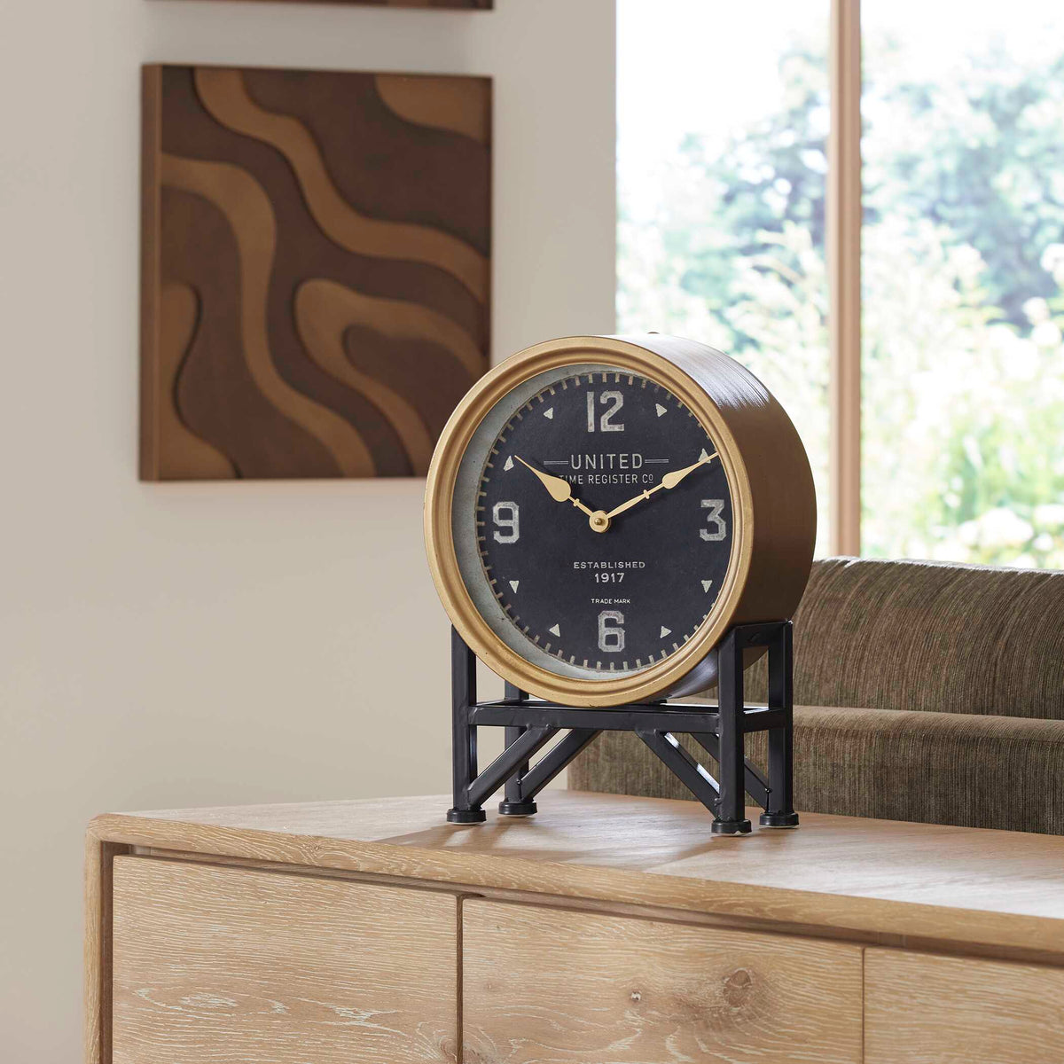 Shyam brass desk clock on a light wood sideboard beside a living room sofa
