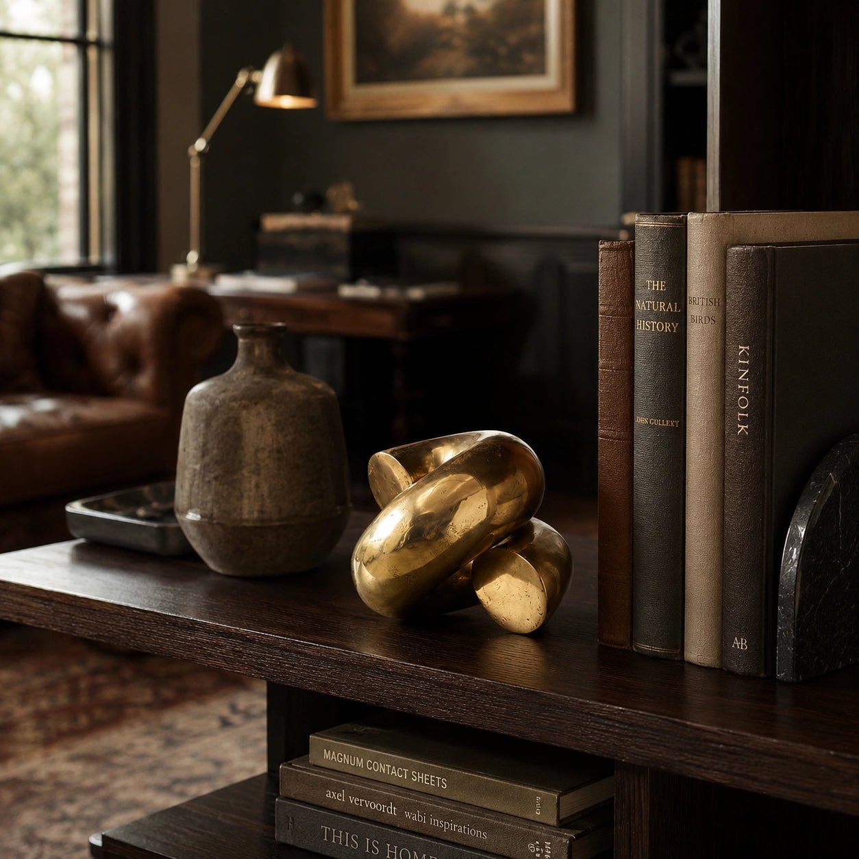 Decorative objects on a wooden shelf in a cozy room with books and a lamp.
