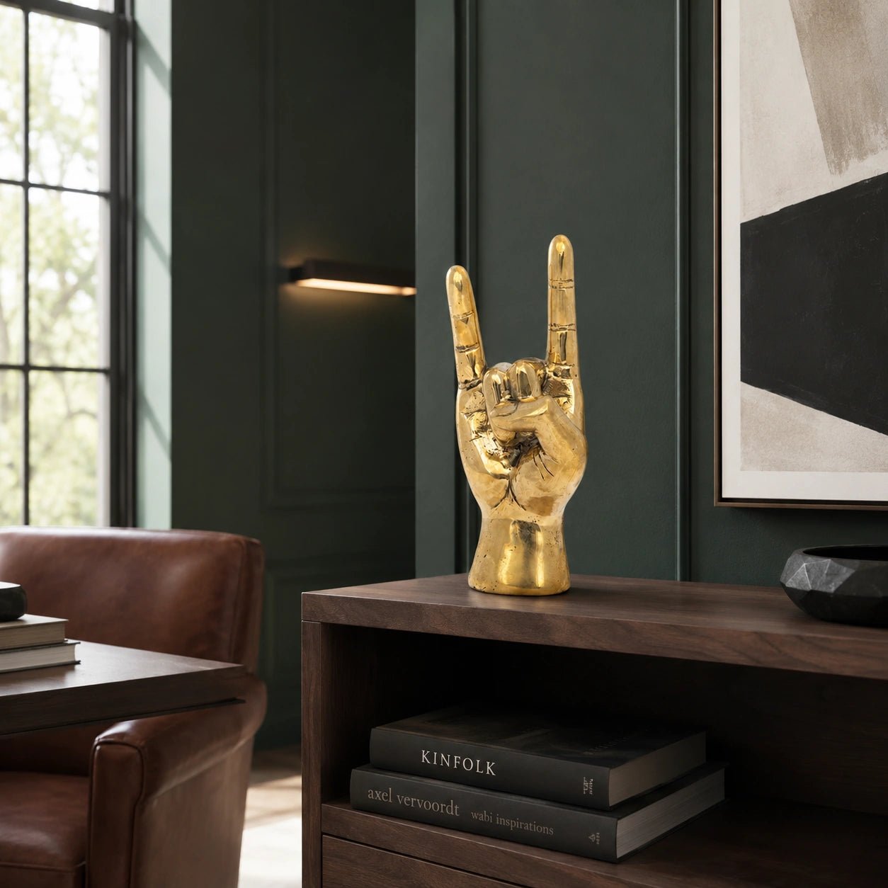 Gold hand sculpture on a wooden shelf with books and a modern wall art piece in the background.