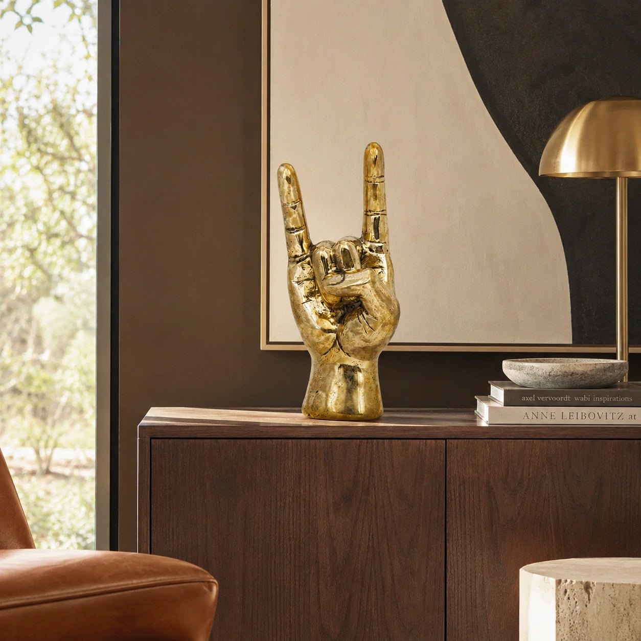 Gold hand sculpture on a wooden cabinet with a mirror and books in the background
