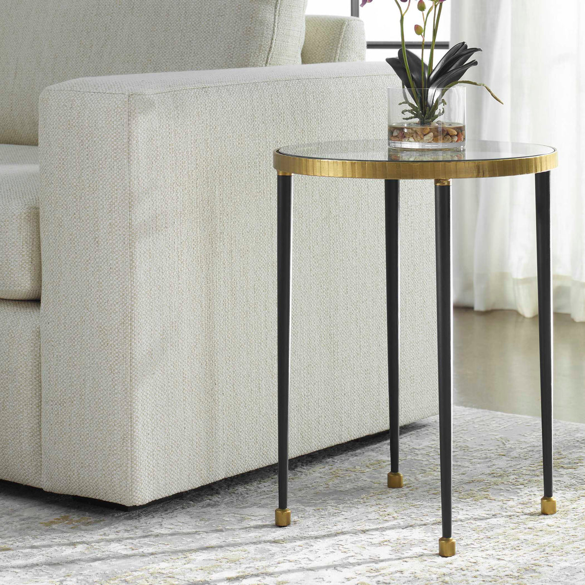 Uttermost 22965 Stiletto side table beside an ivory woven sofa, orchid in a glass vase on top