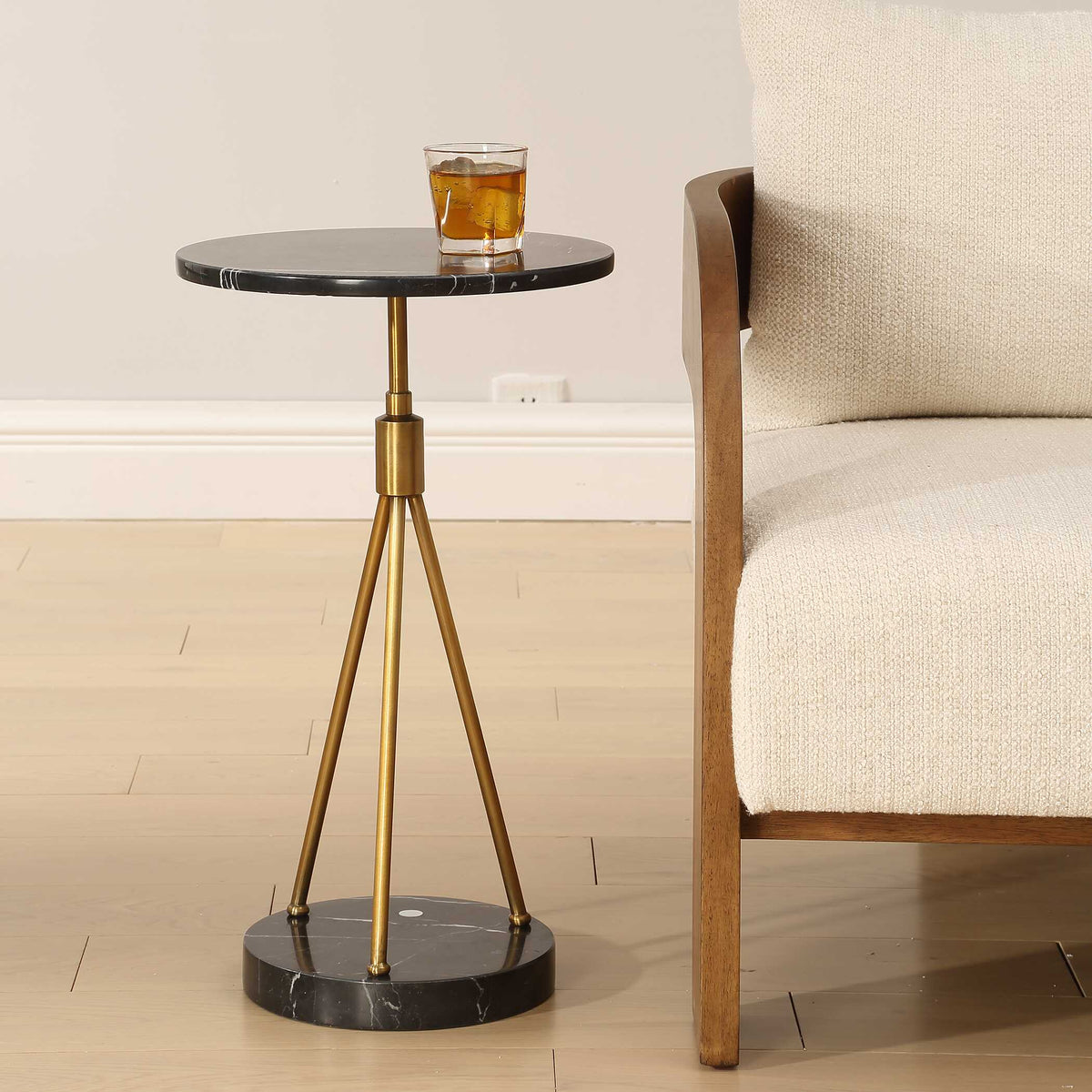 Small marble side table with brass tripod legs next to a wood frame lounge chair, Art Deco living room