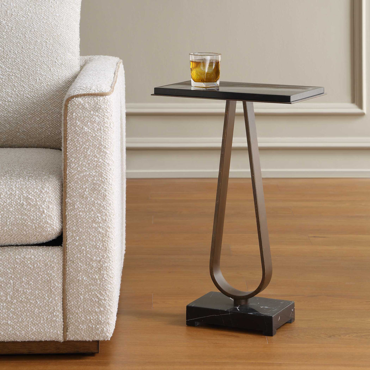 Black marble drink table beside a boucle armchair with a whiskey glass on top, wood floor