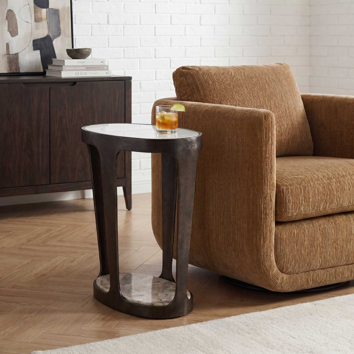 Uttermost 50645 Coronado accent table with a cocktail beside a swivel lounge chair and a white brick wall