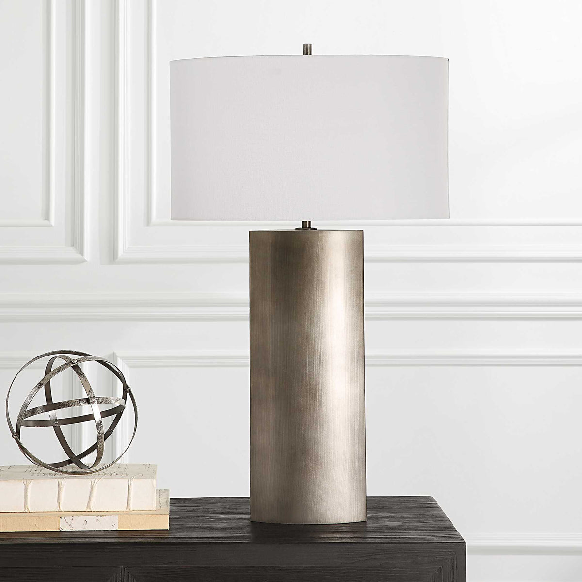 V-Groove iron table lamp on a black console with a metal sphere sculpture and stacked books in a paneled room