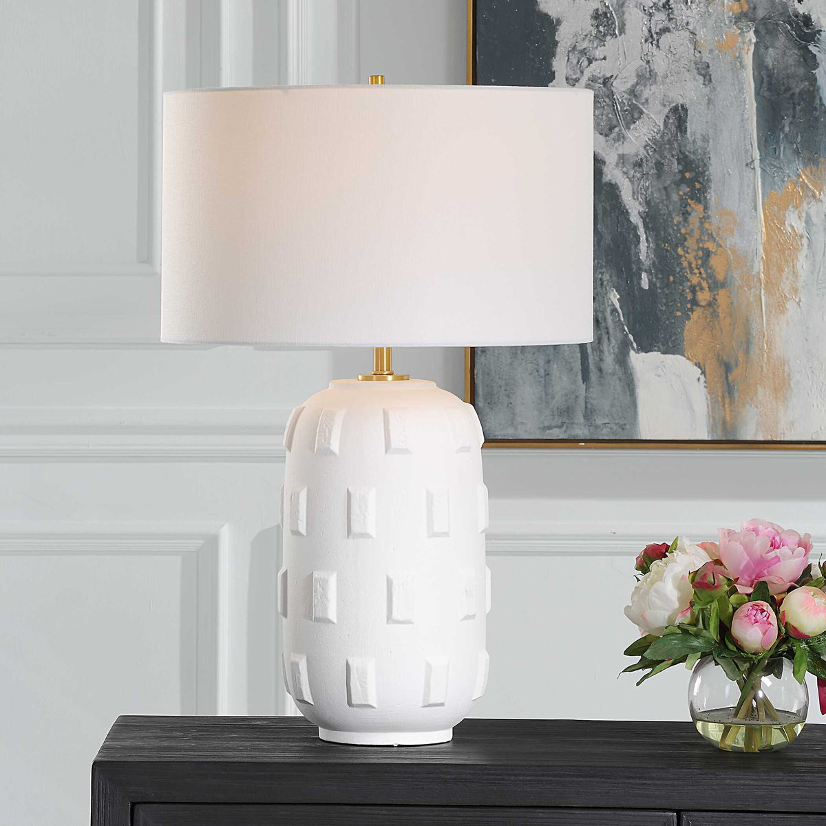 Emerie white porcelain table lamp with raised brick pattern on a dark cabinet beside pink peonies and abstract art