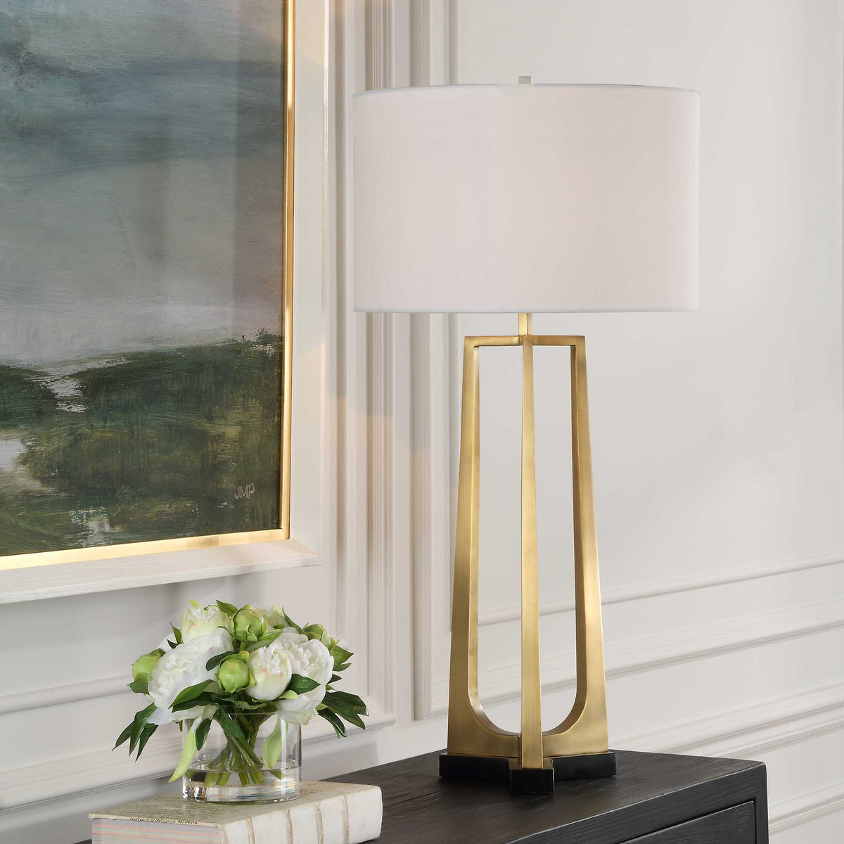 Crossroads antique brass tripod table lamp on a dark wood console under a framed landscape