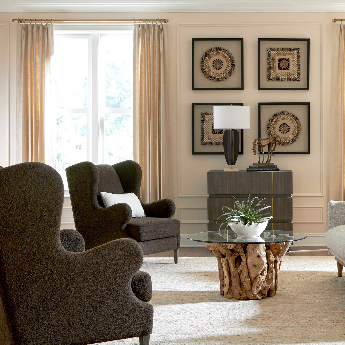 Black sculptural lamp on a gray dresser in a living room with green wingback chairs and wall art