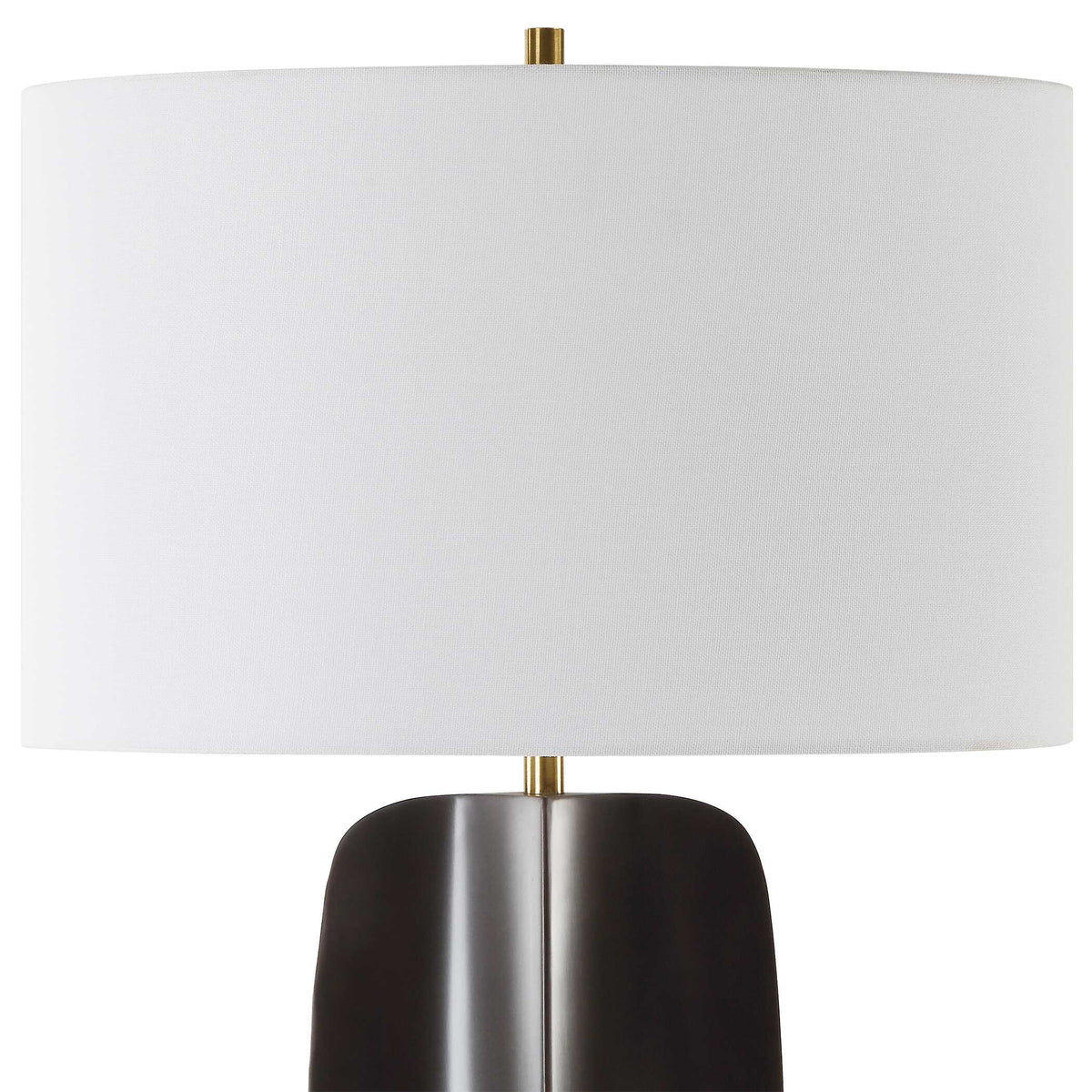 Close view of the oval white linen hardback shade and brass finial on a black iron table lamp