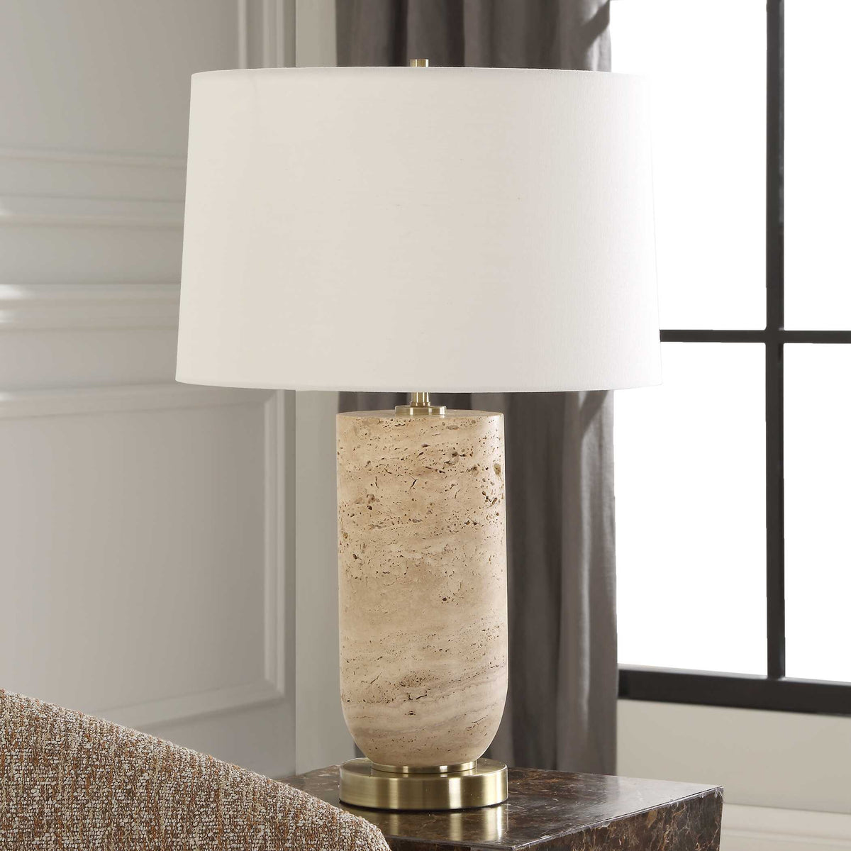 Natural travertine bedside lamp, unlit, beside a tall window with gray curtains and wall paneling