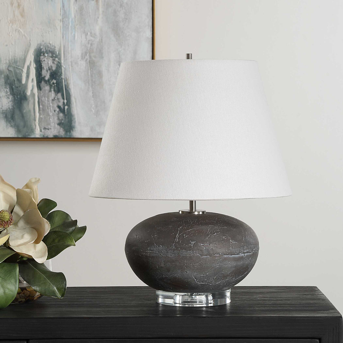 Organic modern nightstand lamp with a round charcoal ceramic base, unlit on a dark wood sideboard