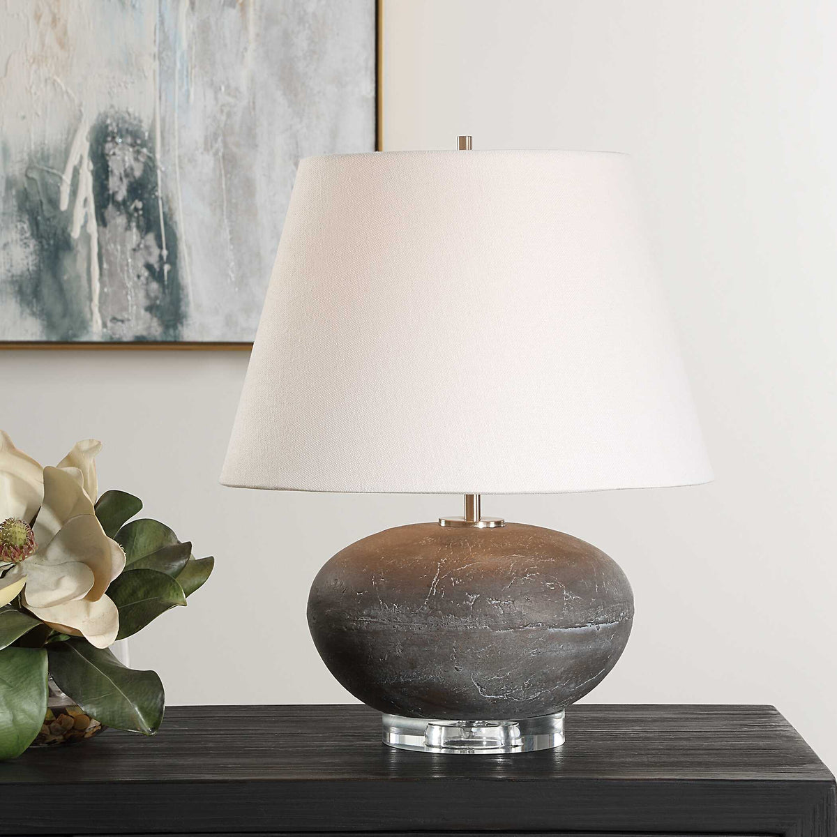 Beckley stone look ceramic table lamp on a dark wood sideboard beside white magnolia blooms