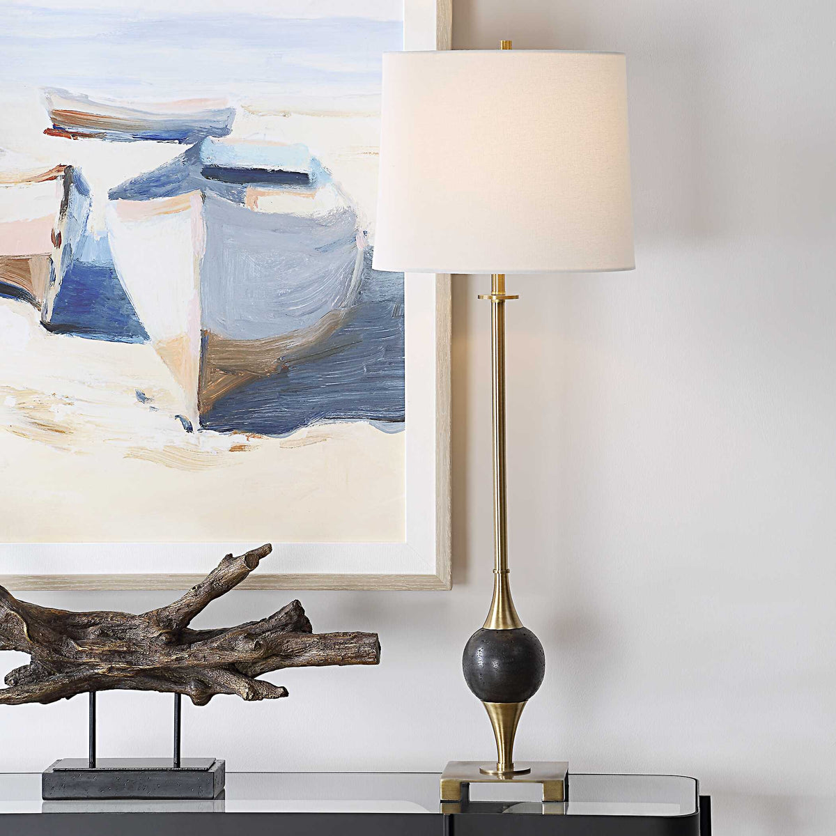 Dempsey buffet lamp lit on a glass top console beside a driftwood sculpture under a coastal boat painting