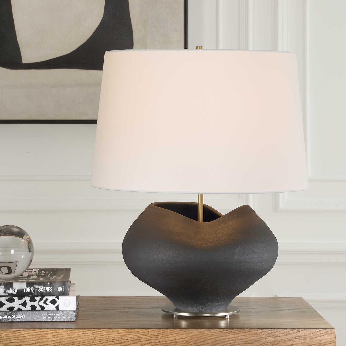 Nocturne Aged Black porcelain table lamp on an oak console beside stacked books and a glass orb