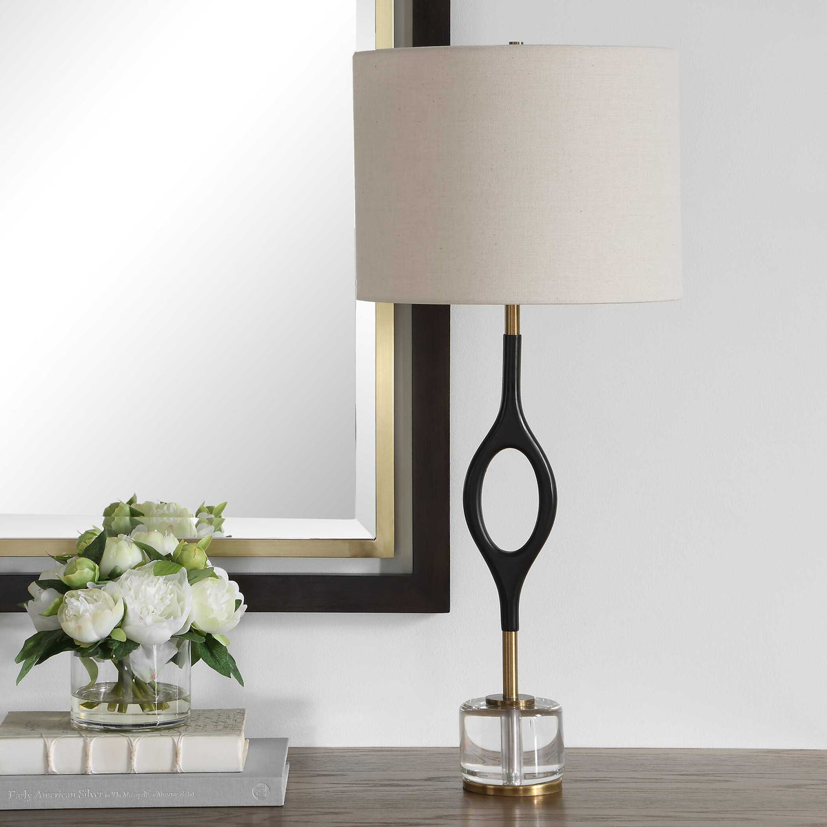 Warm black iron console lamp with open oval silhouette styled on a wood sideboard with books