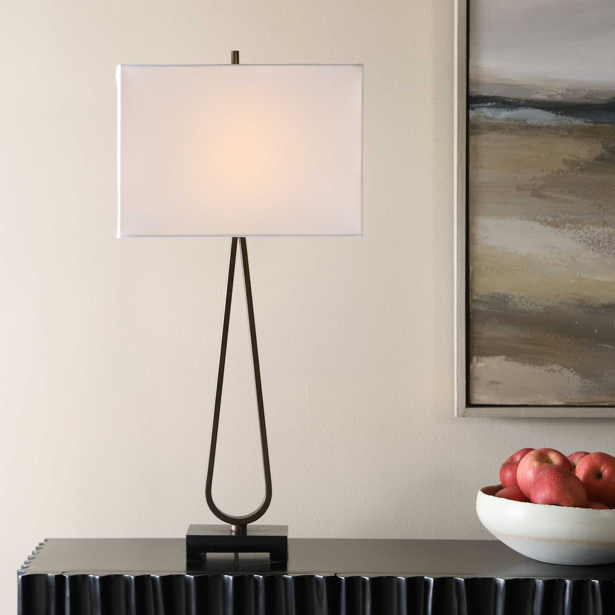 Minimalist slim dark bronze iron bedside lamp with lit rectangle shade beside a white bowl of apples