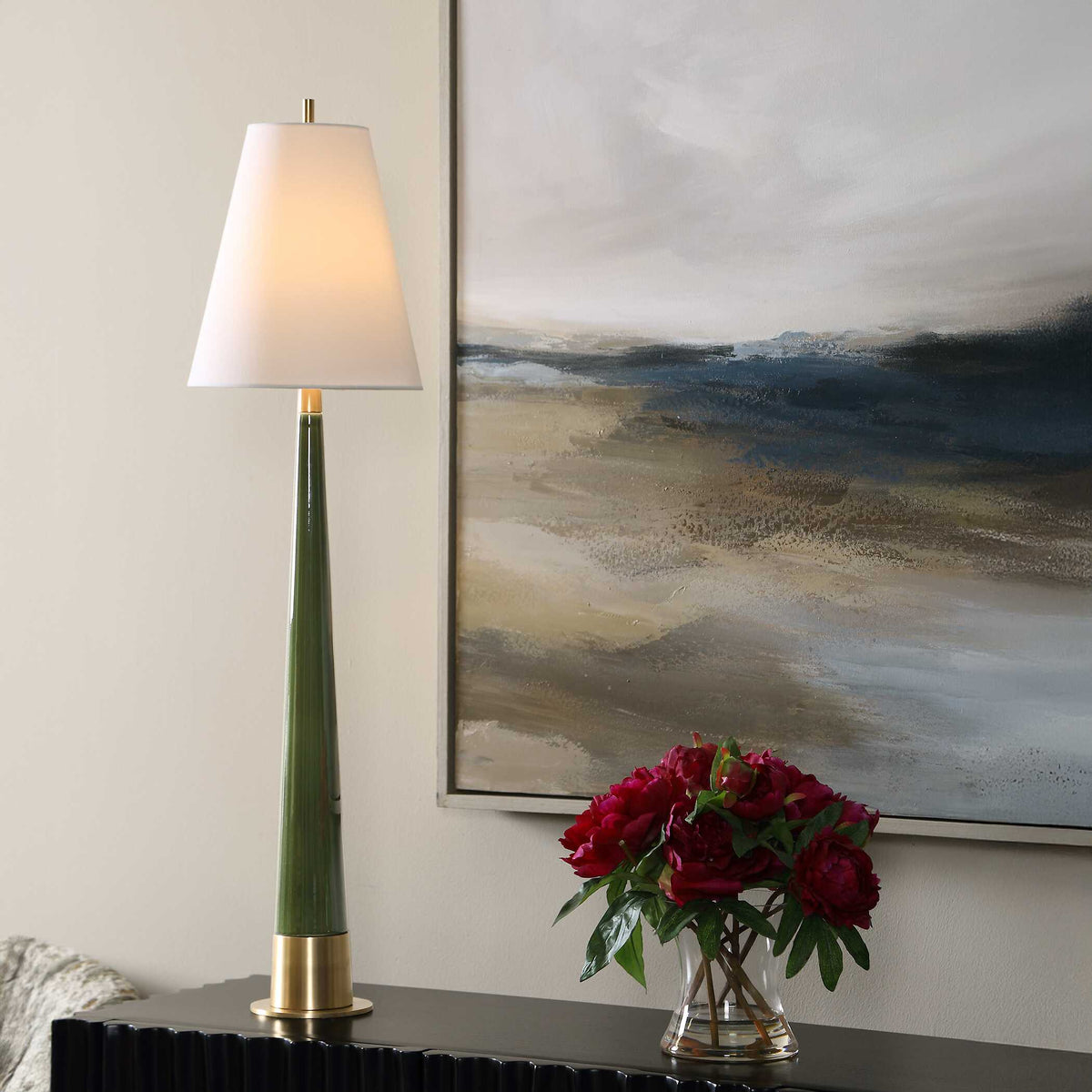 Riccardi tall moss green ceramic table lamp on a black fluted console beside a landscape painting and red peonies