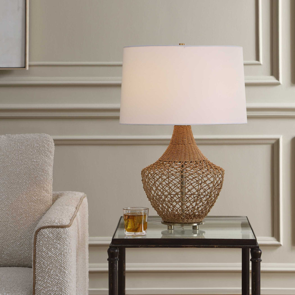 Samori natural rattan table lamp on a glass end table beside a boucle armchair
