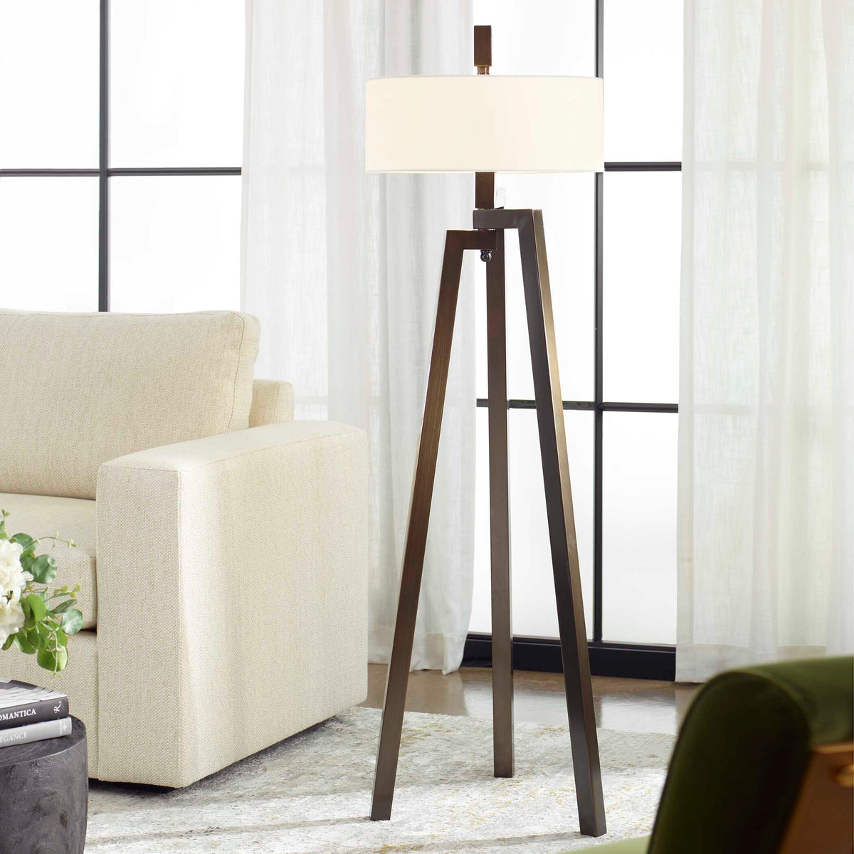 Mondovi hand forged bronze tripod floor lamp beside a cream sofa and steel framed windows