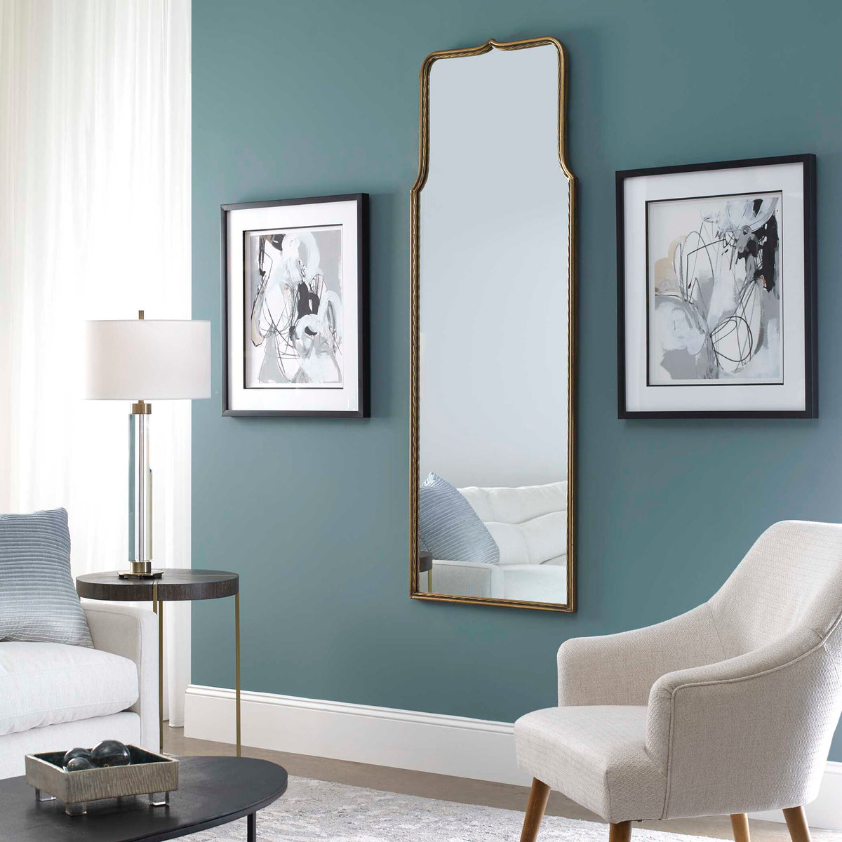 Uttermost 09247 Adelasia gold mirror on a teal wall between framed abstract prints near a white armchair