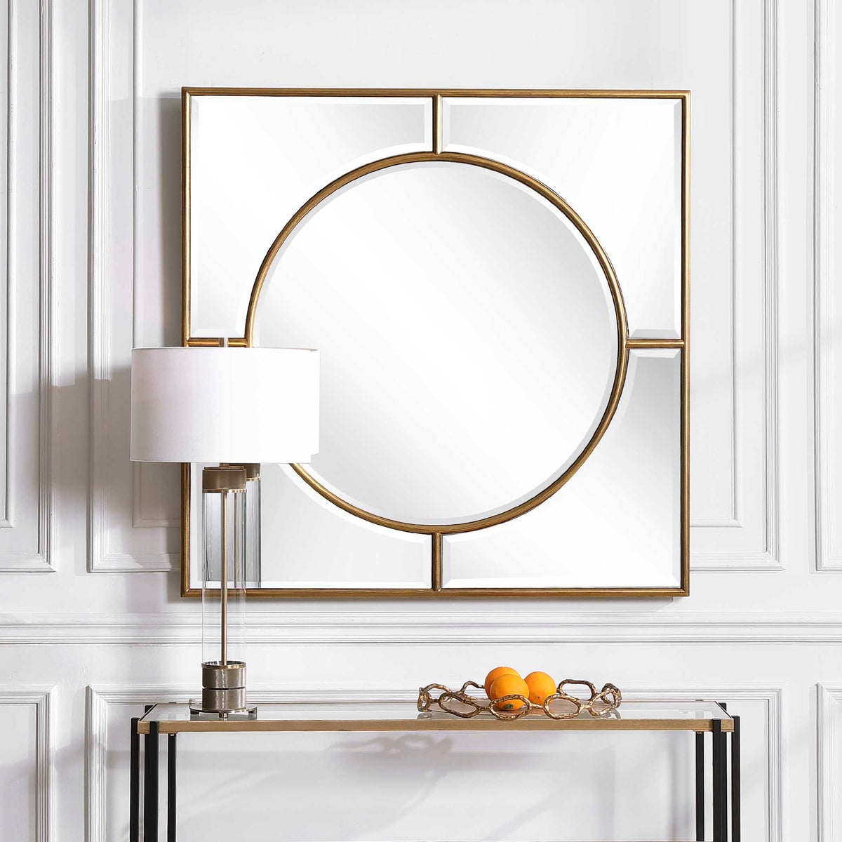 Uttermost 09673 Stanford gold mirror above a glass console table with a lamp and oranges