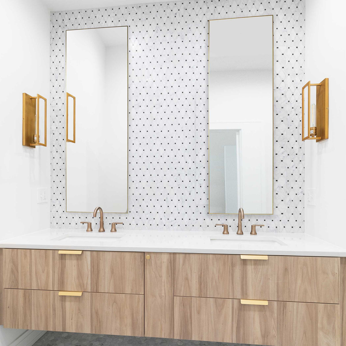 Thin gold frame full length mirrors above a double sink bathroom vanity with gold wall sconces