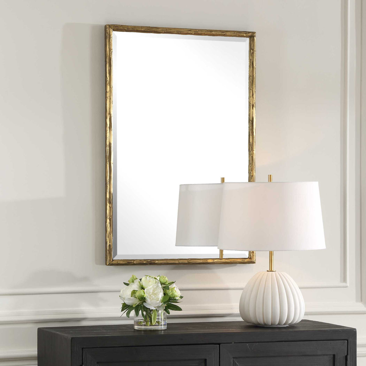 Textured gold rectangle mirror above a sideboard with white flowers and a lamp