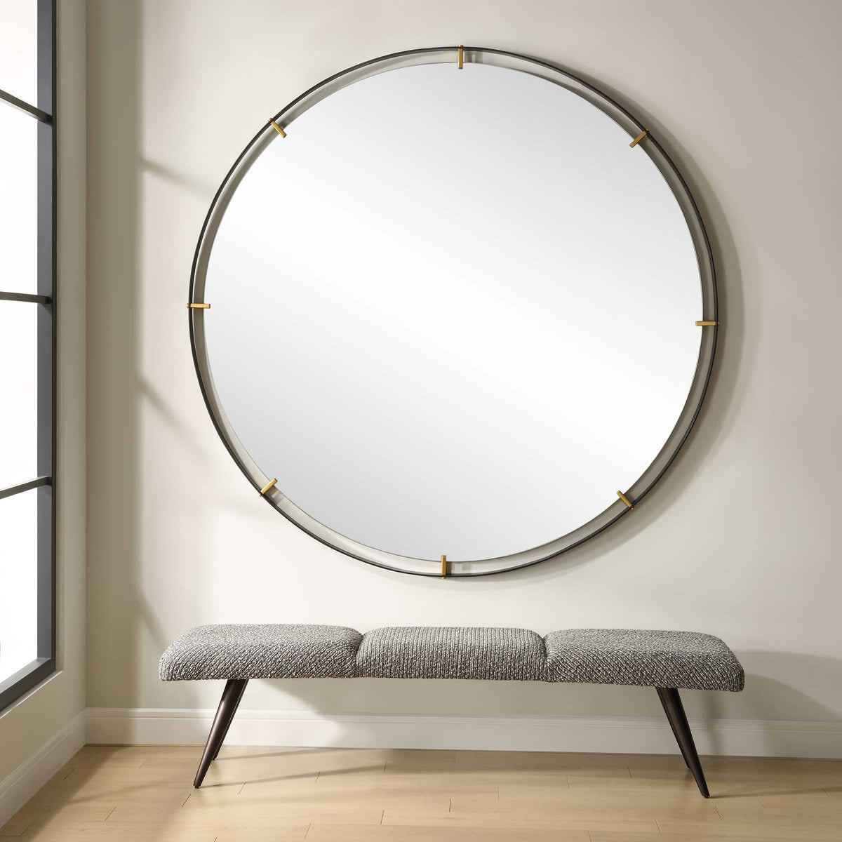 Huge circle wall mirror hung over a bench beside tall windows