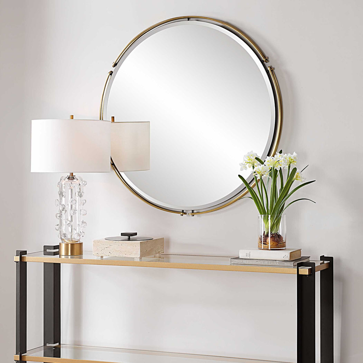 Round brass mirror over a console with a lamp and flowers, alternate view