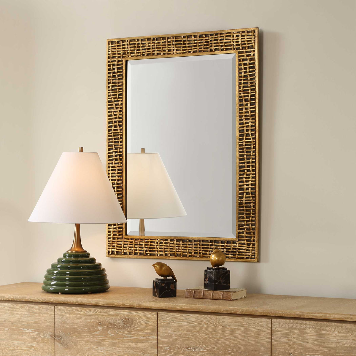 Woven gold accent mirror over a sideboard with brass figurines, angled view