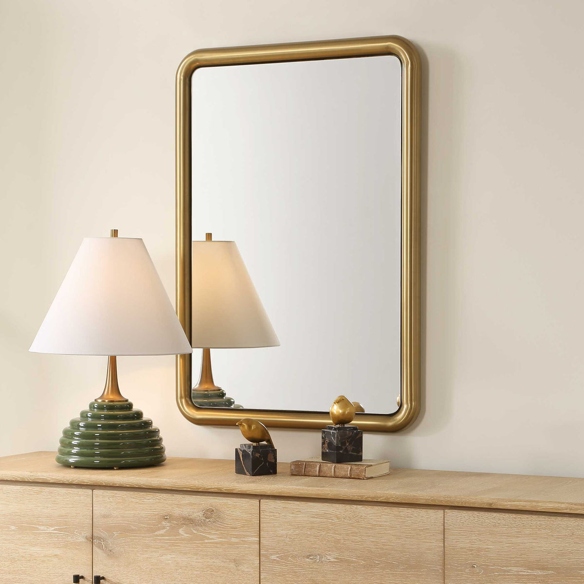 Rounded corner wall mirror in antique brass, angled above a credenza with a ribbed lamp