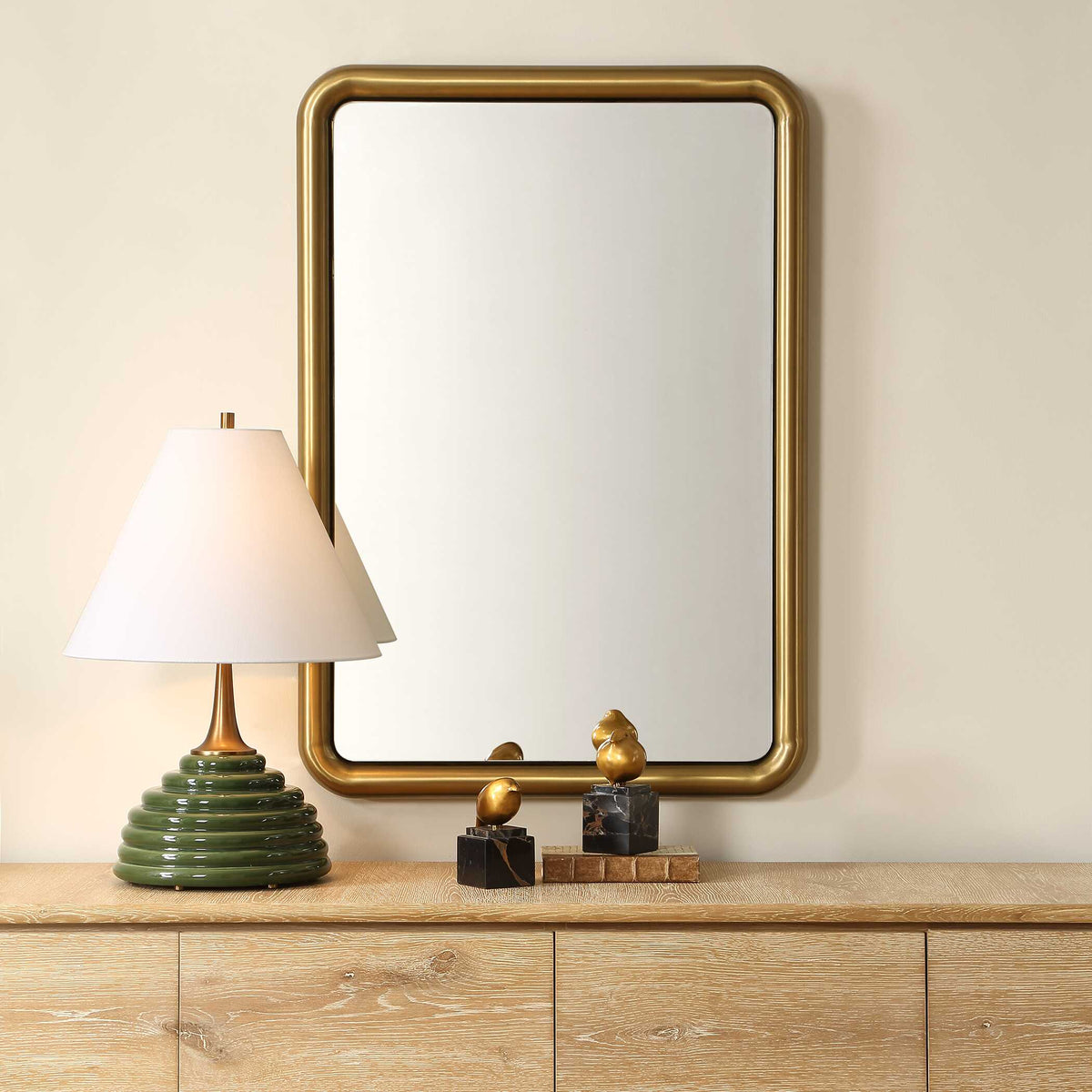 Uttermost 08317 Atkinson collection brass mirror above a light wood credenza with a green table lamp