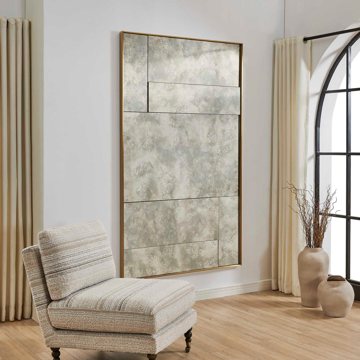 Large antique style mirror with pieced glass panels hung beside a striped slipper chair and arched window