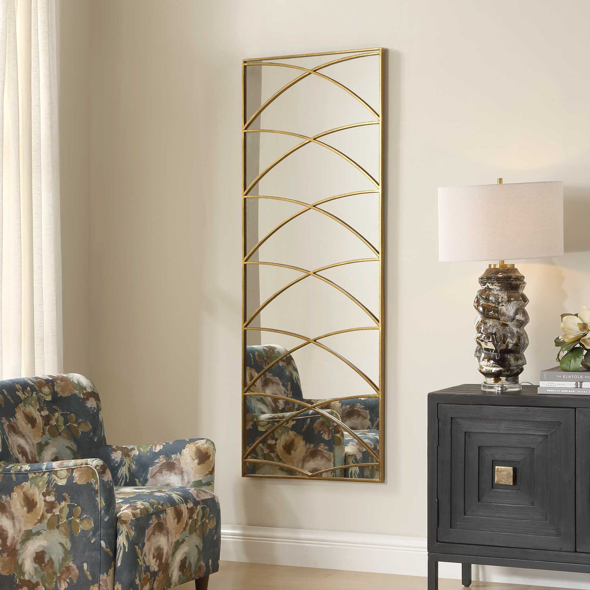 Tall gold wall mirror with an arch pattern overlay, angled view reflecting the armchair