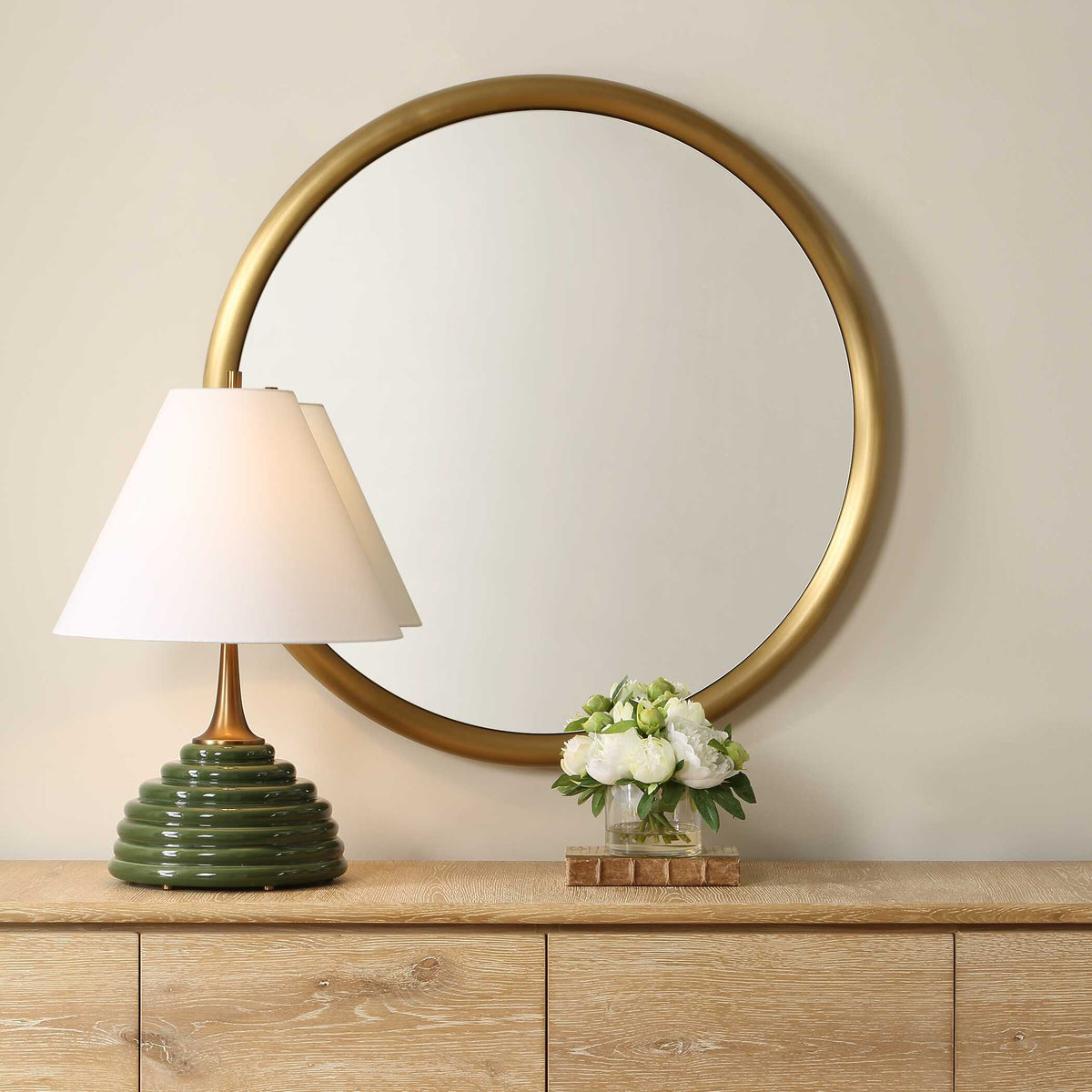 Uttermost 08335 Atkinson collection round brass mirror above a light wood credenza with a green lamp