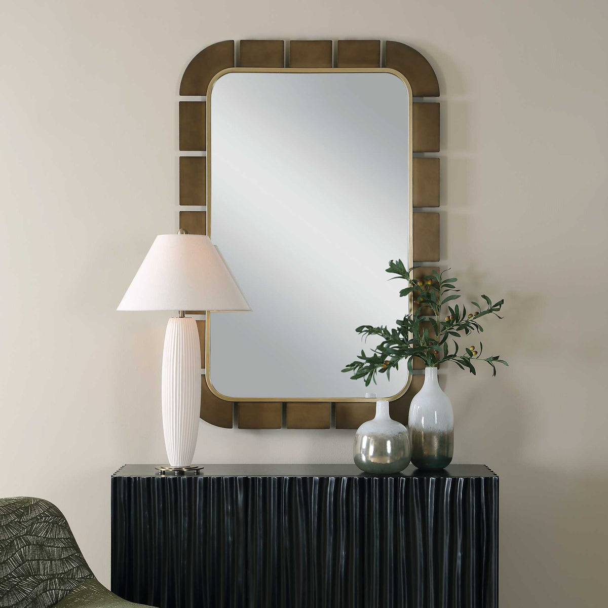 Uttermost 08378 Segment collection mirror above a fluted dark sideboard with a white lamp