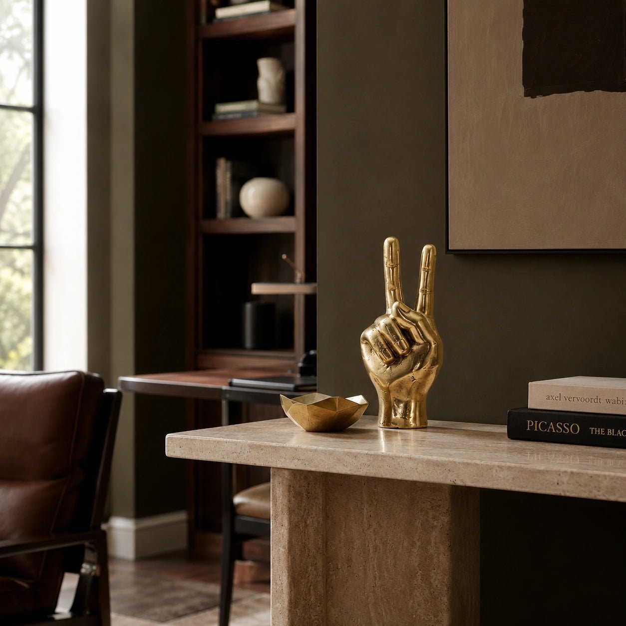 Gold hand sculpture on a table in a room with books and a painting.