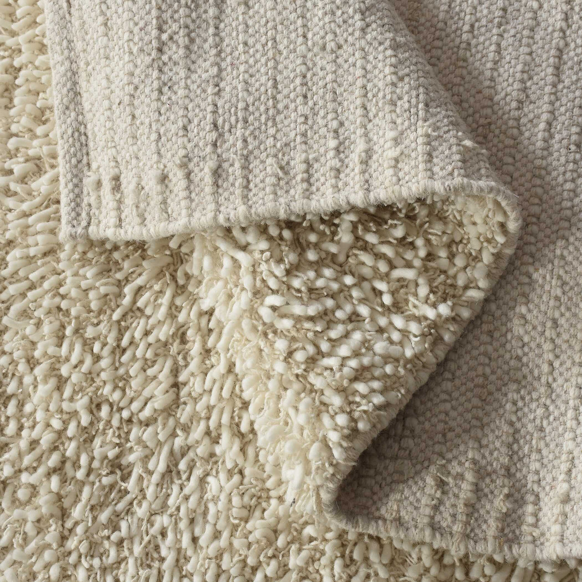 Folded corner of an ivory wool shag rug showing the woven backing and thick pile