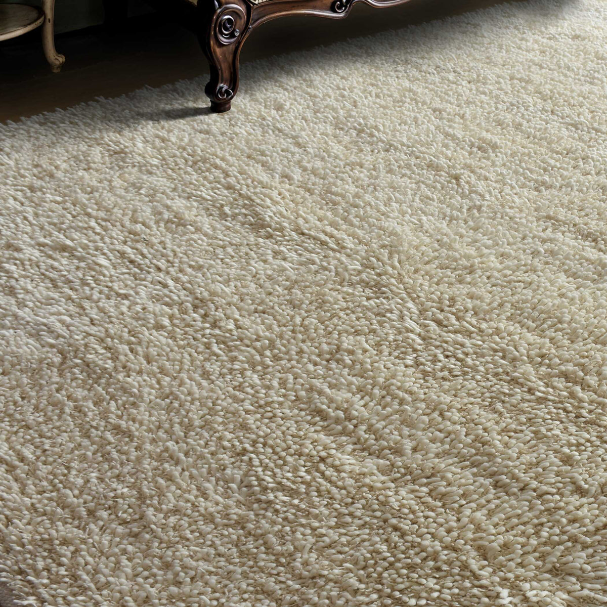 Caramont ivory shag rug beside a carved dark wood furniture leg