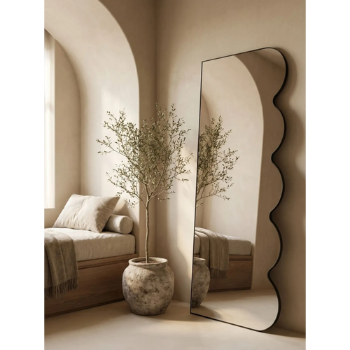 Black floor mirror leaning in a sunlit plaster nook