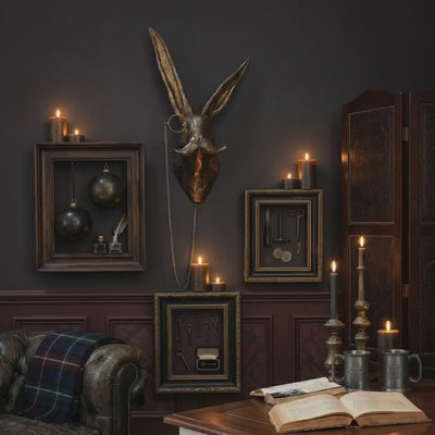 product video of an Eric the Hare cast aluminum antique gold wall mount used as gold-wall-decor in a moody study with framed curiosities and candles